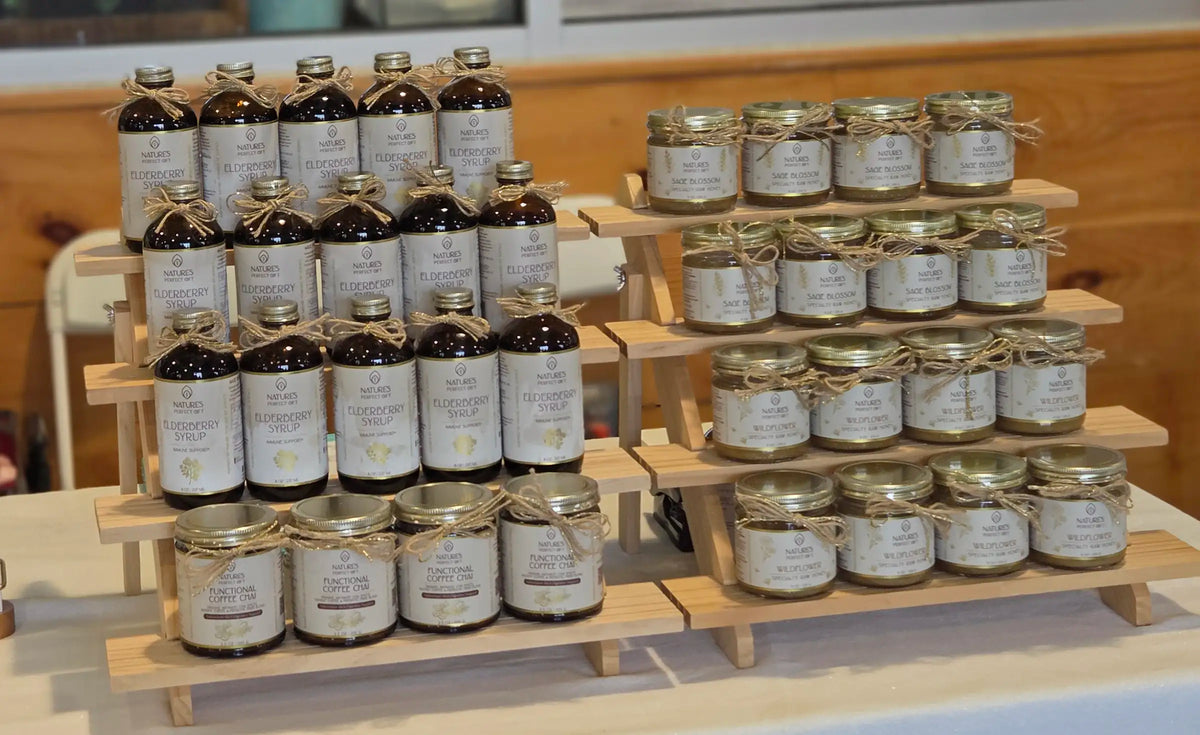 Two wooden display stands holding multiple glass jars and bottles with white labels and gold lids, arranged on a table in an indoor setting.